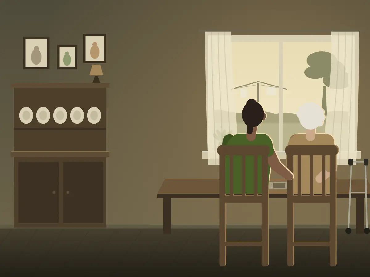 A support worker and her client sit together at a kitchen table by an open window.