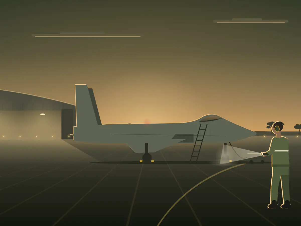 An Air Force aircraft technician in ear defenders shines a torch on the nose gear of a jet on the flight line at dusk.